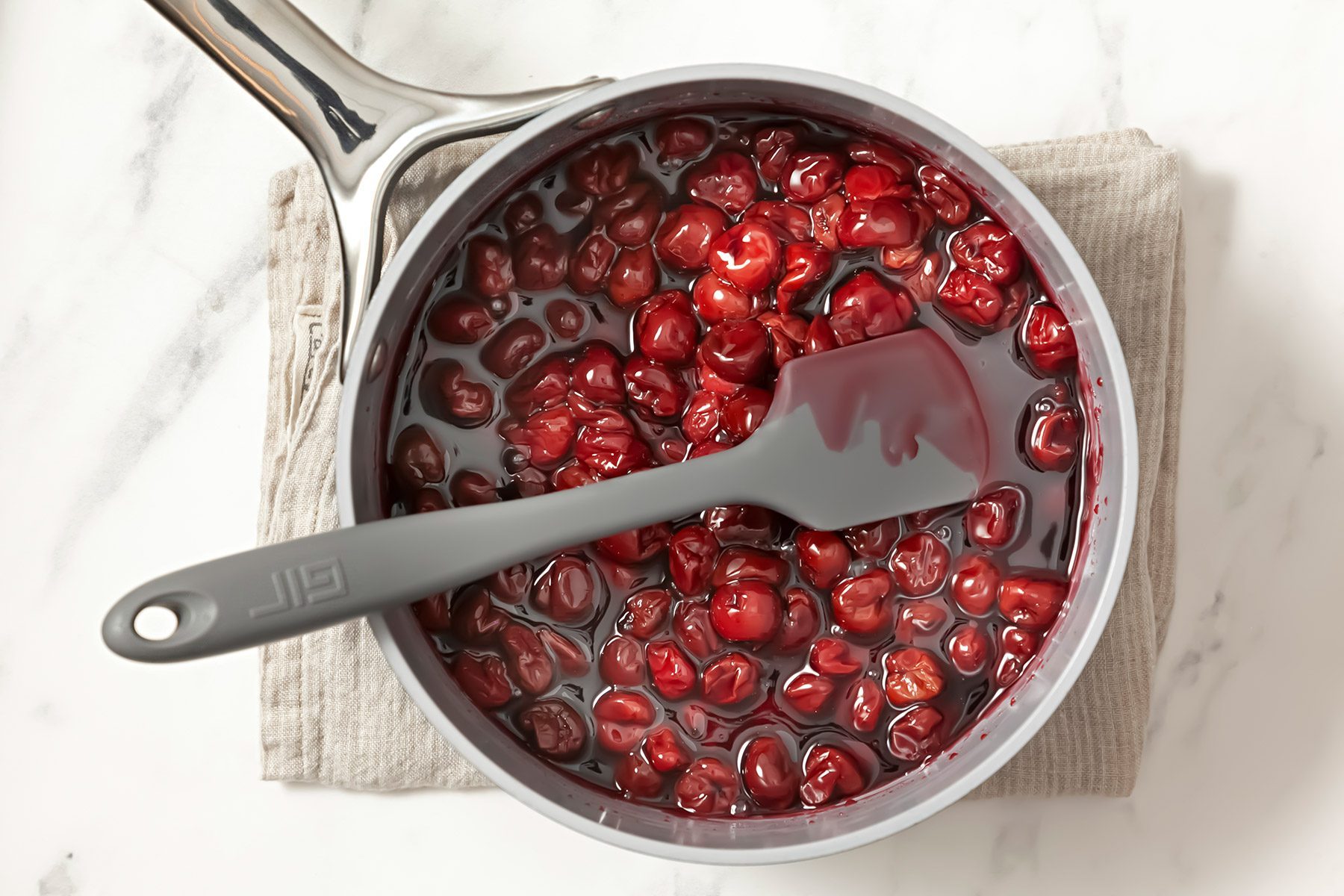 overhead shot; white background; in a large saucepan cherries in cherry juice; saucepan over kitchen towel