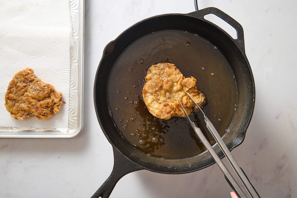 Image of chicken fried steak being fried in oil in a cast iron skillet
