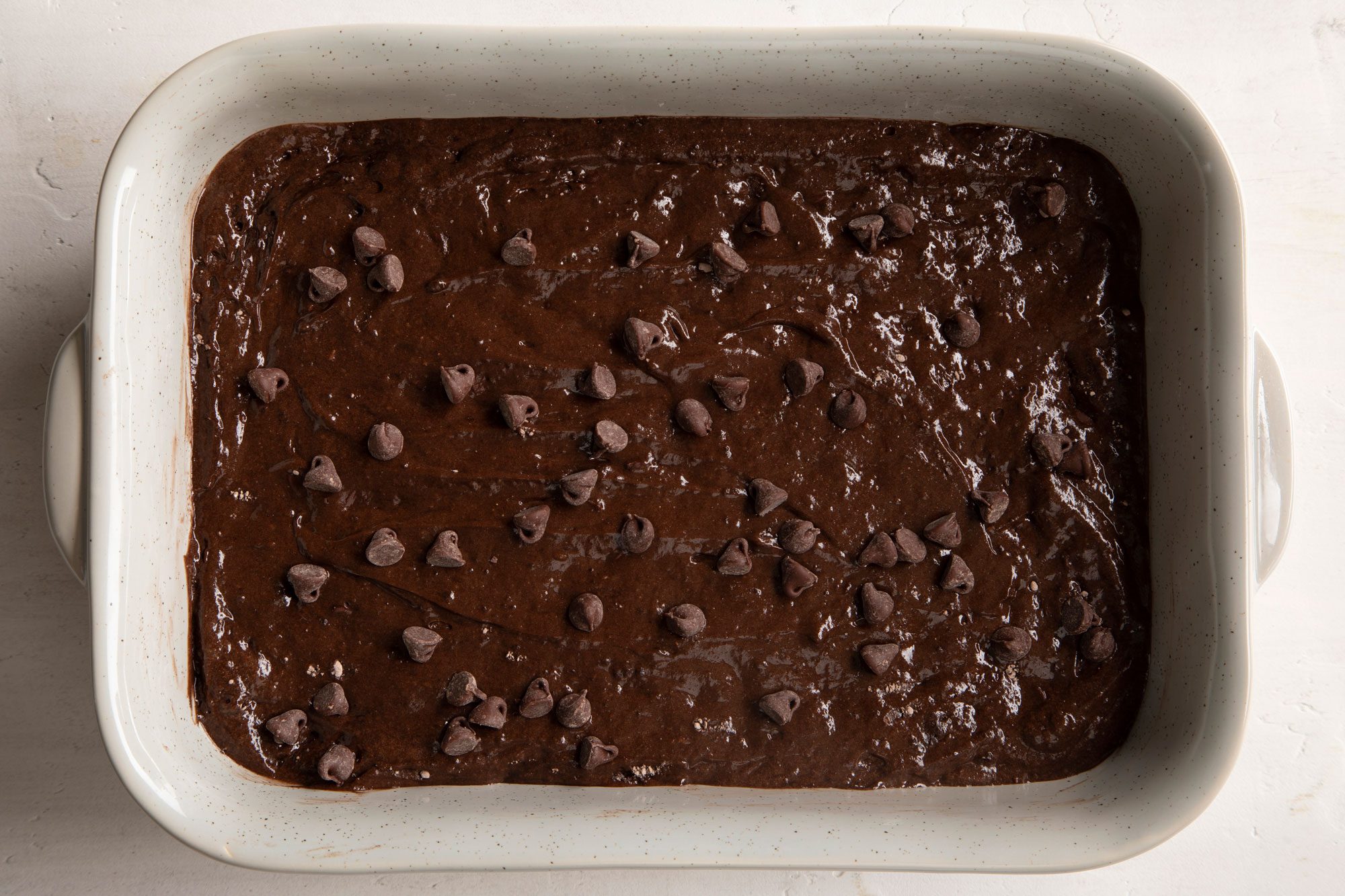 Chocolate Dump Cake mix topped with chocolate chips in a rectangular baking dish