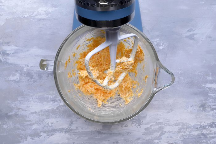 A hand mixer blending butter and cheese in a mixing bowl.