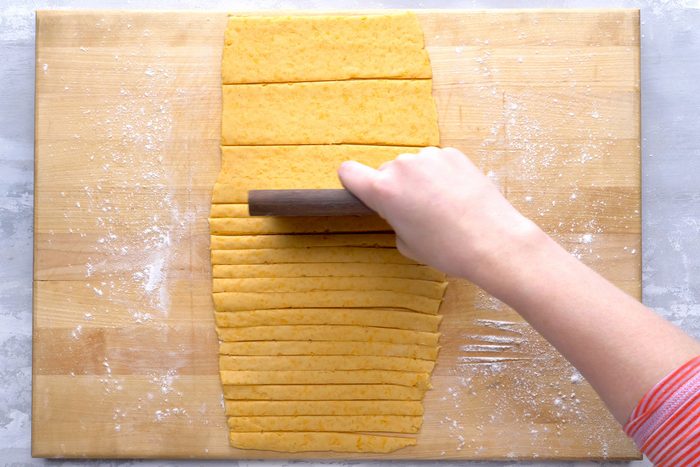 A hand cutting the dough using a bench scraper.
