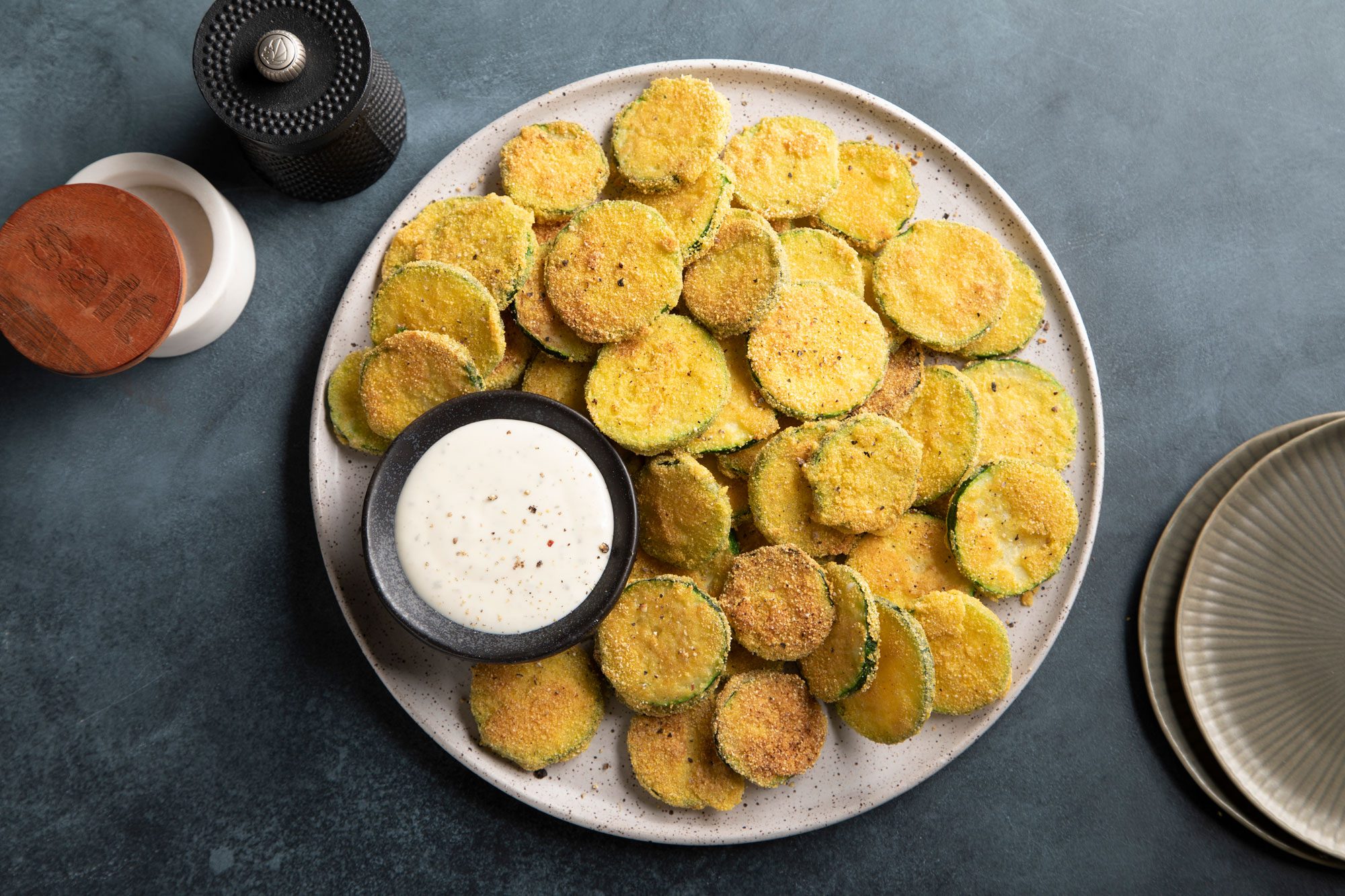 Overhead shot of Fried Zucchini served on a round plate on a dark background