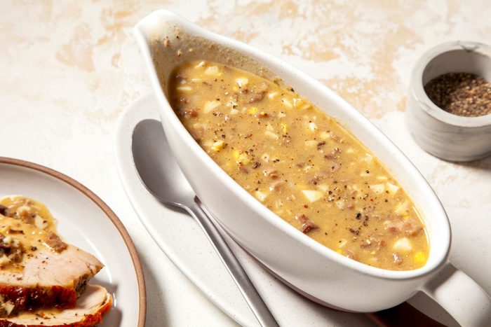 Turkey Giblet Gravy served in a fancy bowl with gravy poured over slices of roast turkey breasts and mashed potatoes