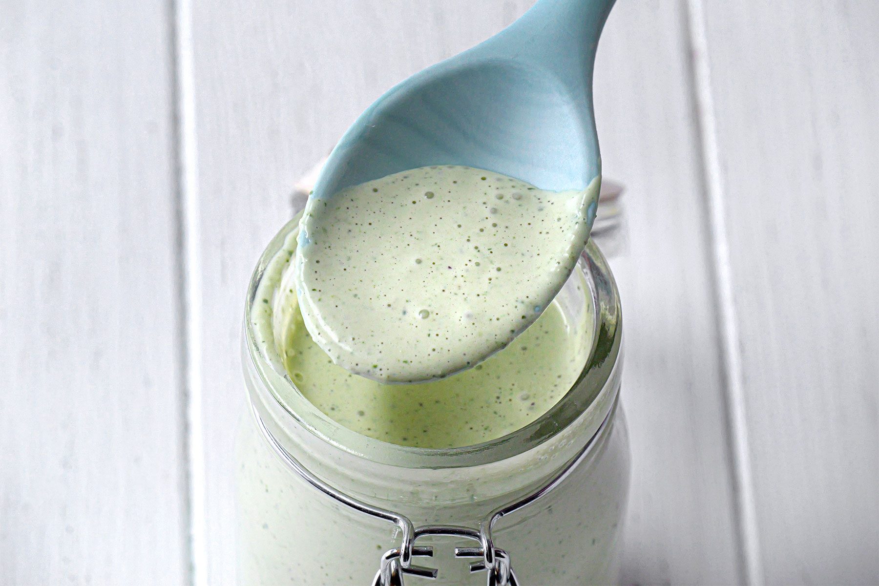 High angle shot of Green Goddness Dressing; in a glass jar; spoon; white wooden background;