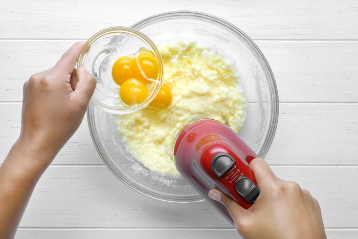 Overhead shot of aded eggs; beat until well blended; blending machine; white wooden background;