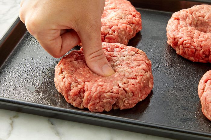3/4 angle view shot of shape use your thumb to press a divot in the middle of each patty; arrange on a greased in baking sheet; marble background;