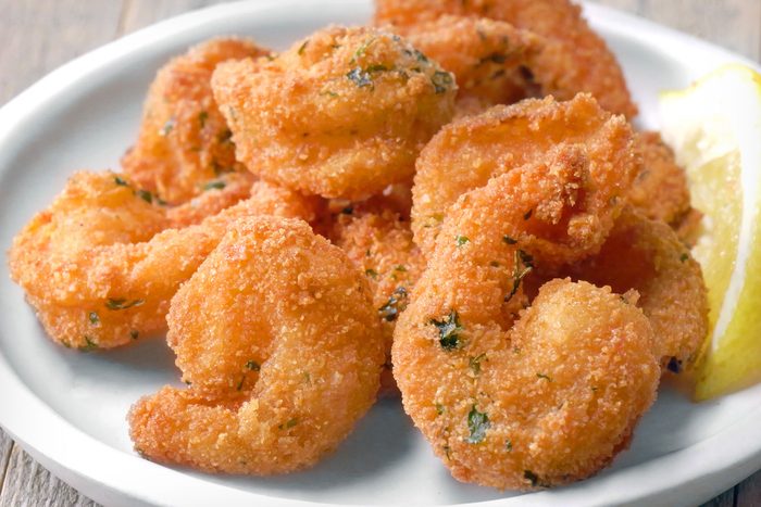 Close shot of Popcorn Shrimp; served on plate with sauce and lime wedges; wooden background;