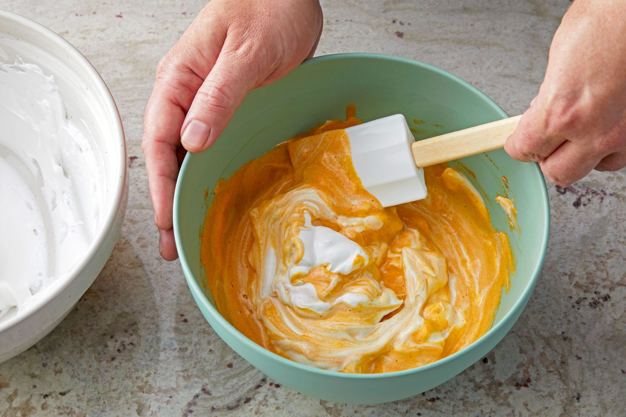 3/4th shot; white textured background; in a small bowl mixing pumpkin mixture and cheese cream mixture together with spatula;