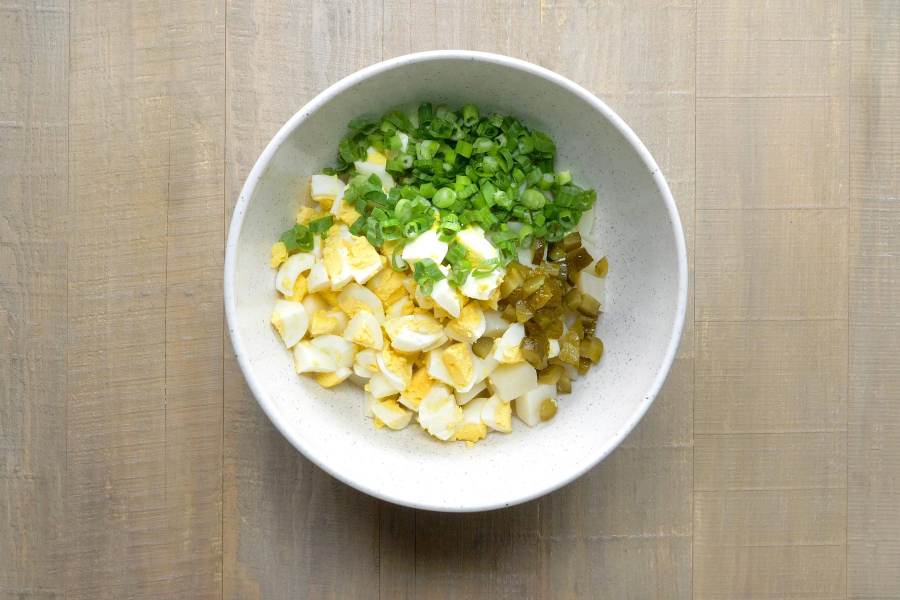 A bowl of potato cubes with onions and pickles.