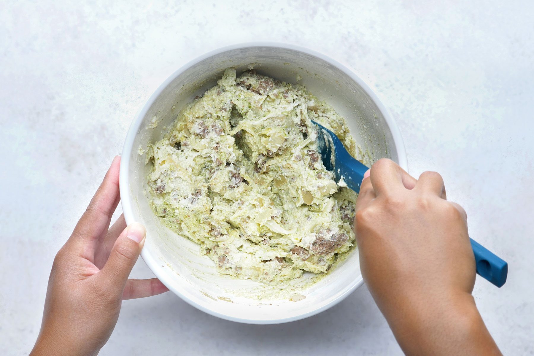 overhead shot; white background; In a large bowl, combining the ricotta cheese, Italian cheese blend, Parmesan cheese, pesto, egg and half of the beef mixture using spatula;