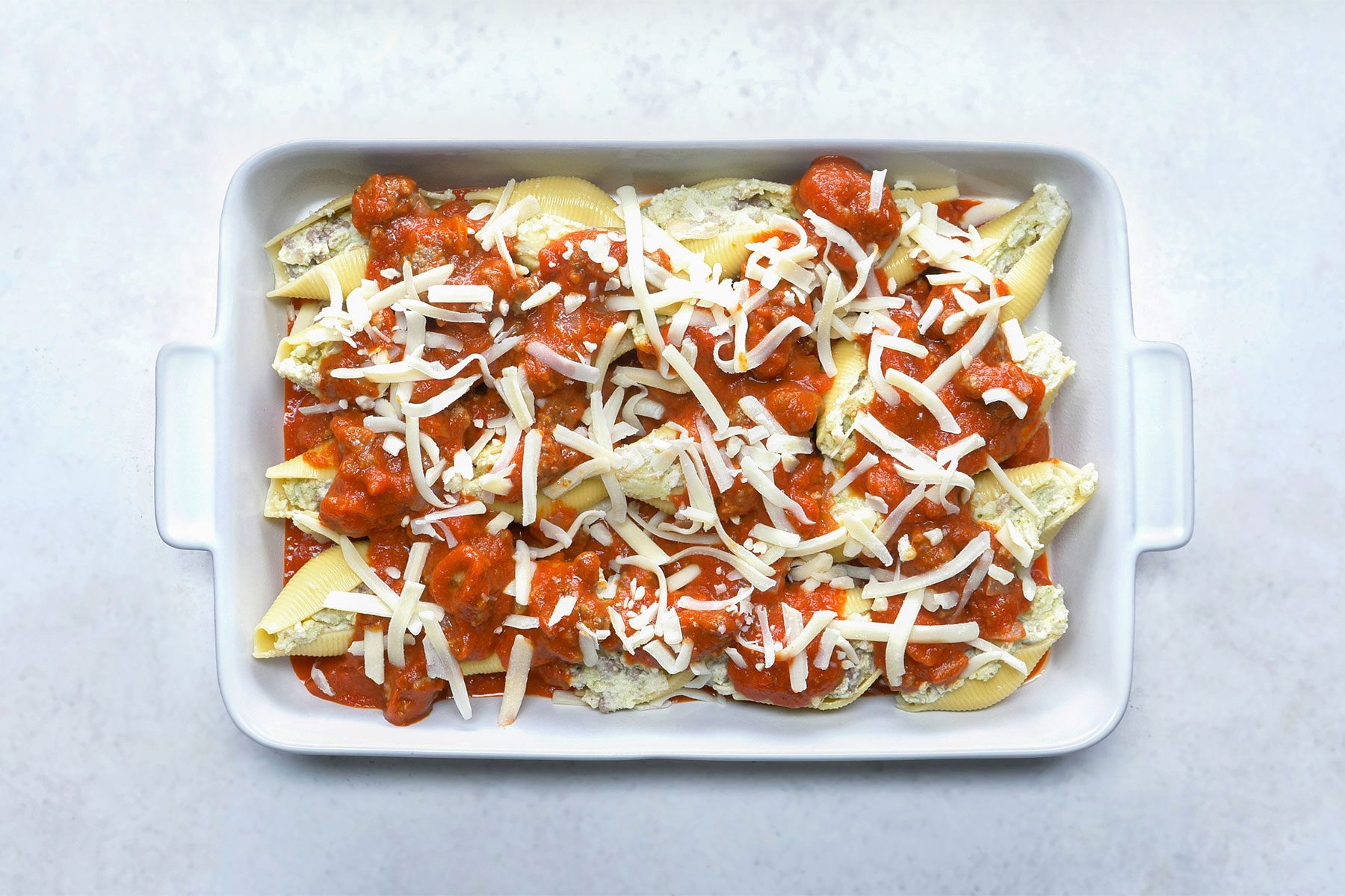 overhead shot; white background; Combining beef mixture and spaghetti sauce using spatula;