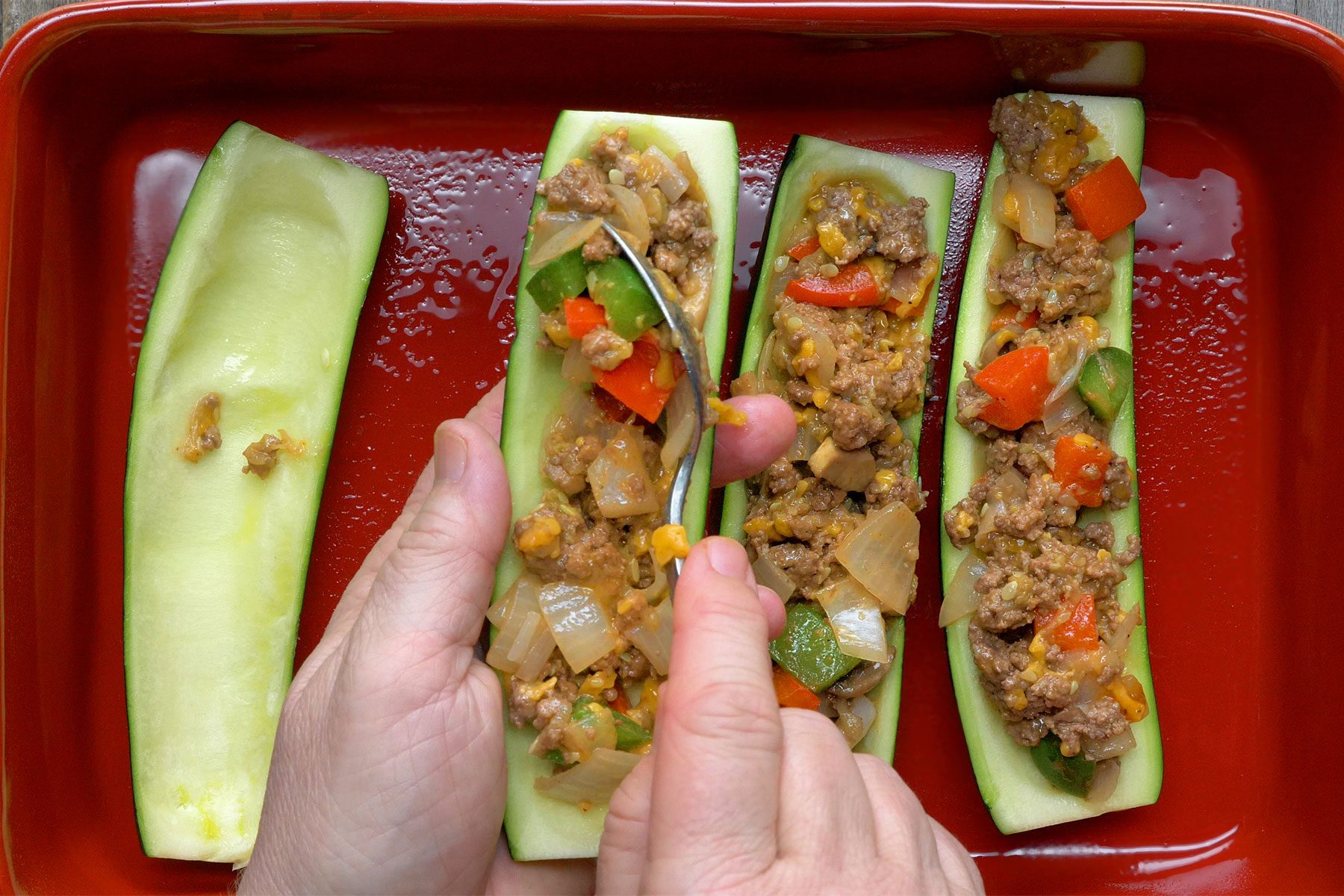 Overhead shot of spoon into zucchini sheels; placed in a greased baking dish; wooden background;