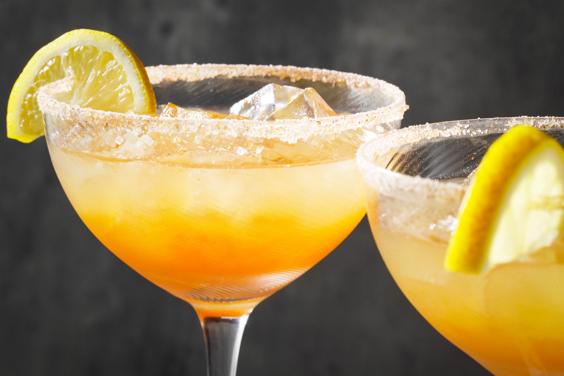 Two glasses of Apple Cider Margarita with a lemon wedge and ice cubes.