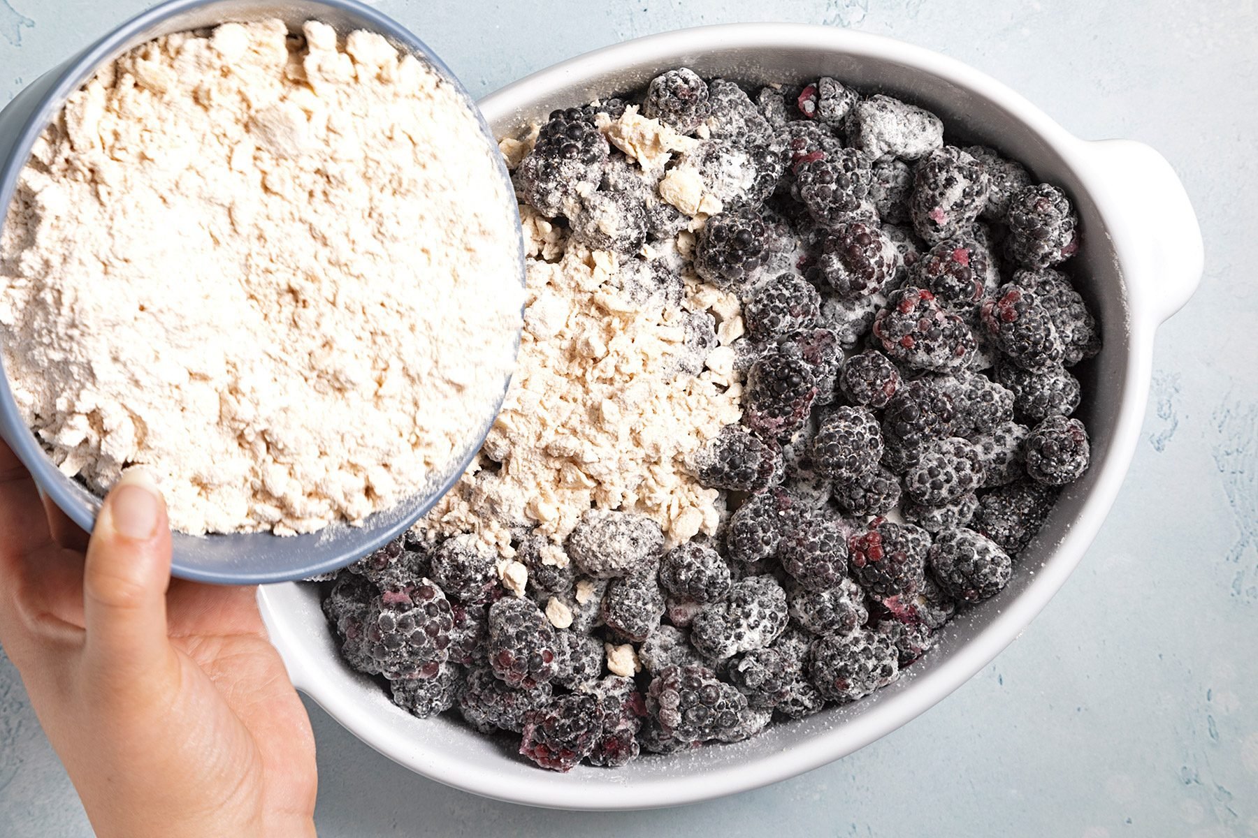 Overhead shot of transfer coated berries into greased baking dish; sprinkle mixture over berries; blue marble background