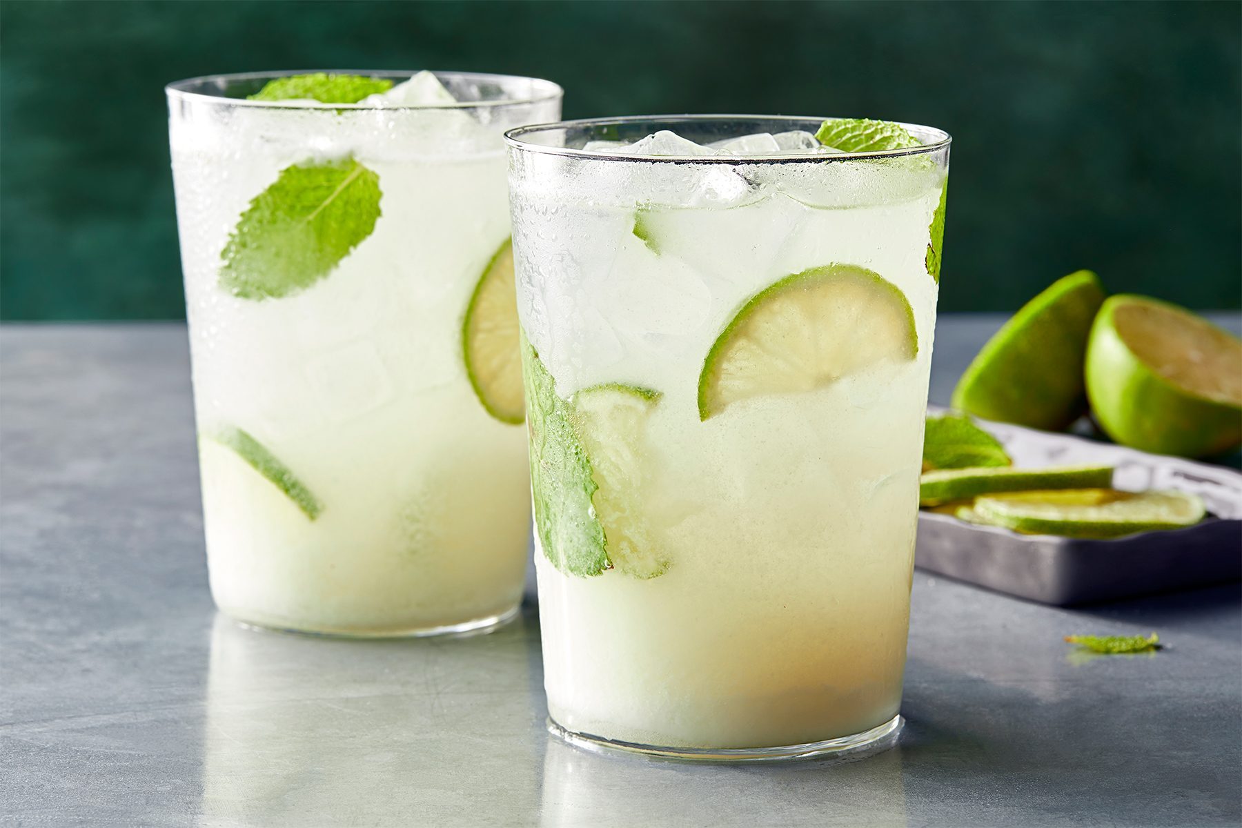 horizontal shot; green background; grey base; Coconut Mojito served into glasses garnished with additional lime and mint leaves