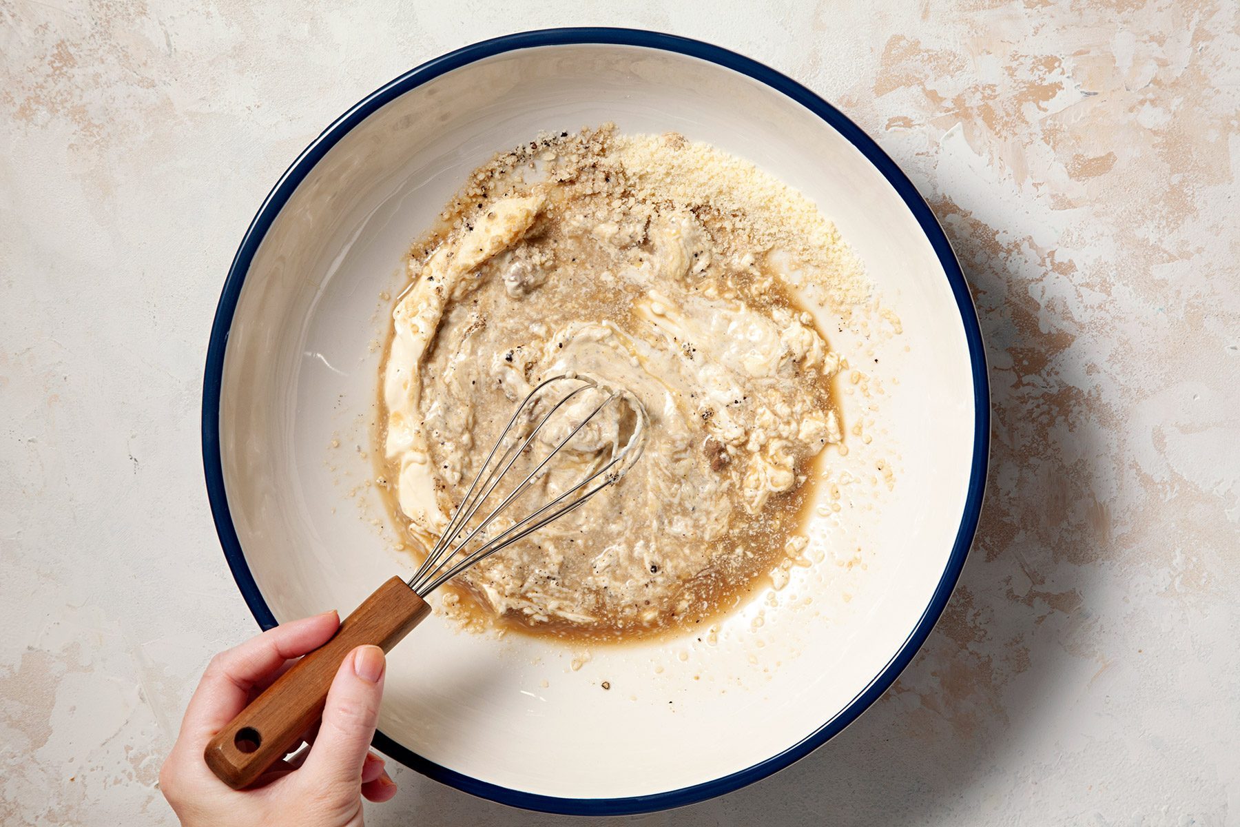 Overhead shot of large bowl; combine olive oil; salt and pepper; mix well; whisk tool; cream marble background