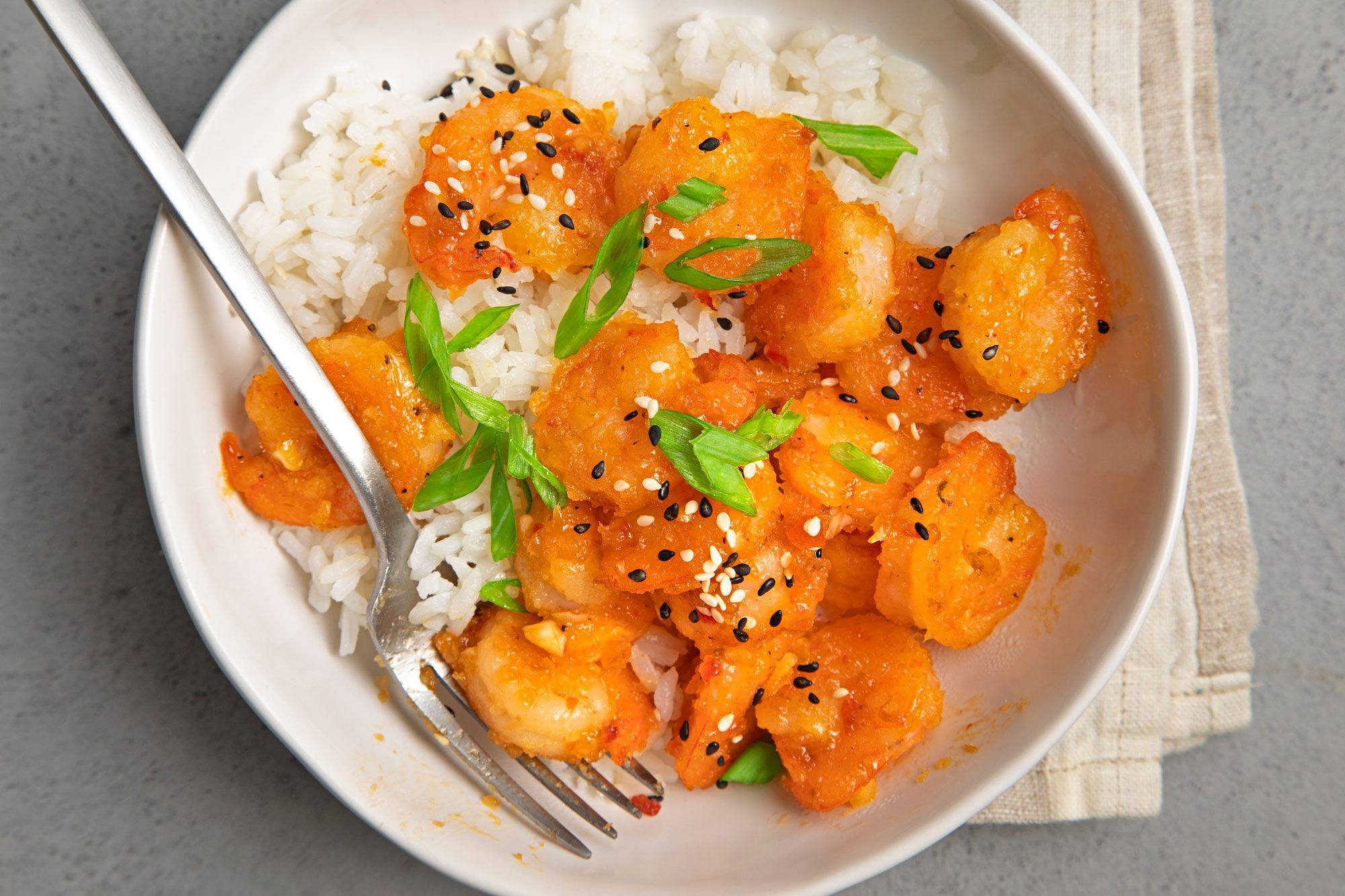 overhead shot of firecracker shrimp served with rice, garnished with sesame seeds and green onions