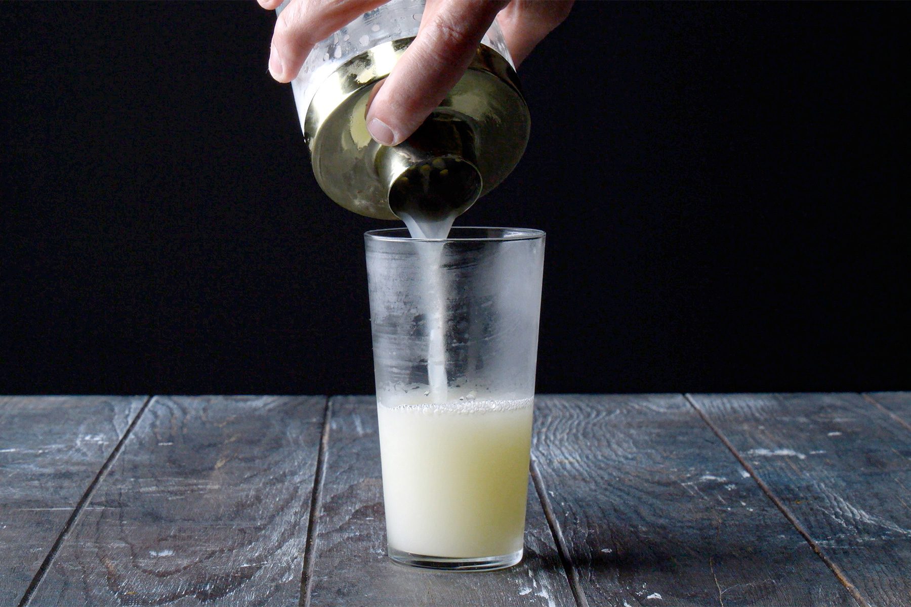 horizontal shot; black background; Straining into chilled highball glass from shaker