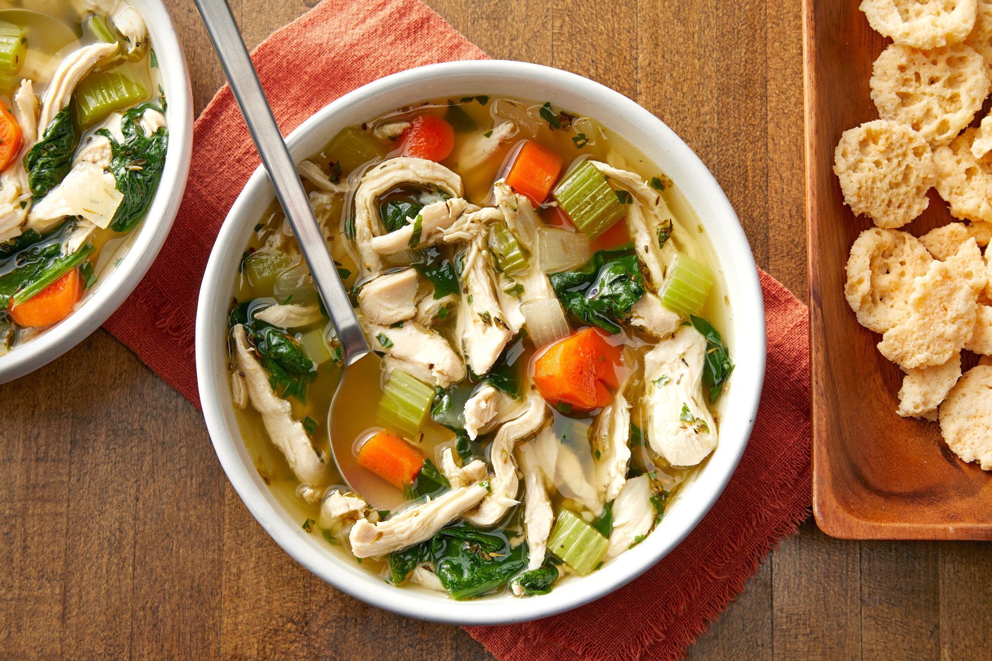 overhead shot of keto chicken soup served in a bowl with cheese crisps; wooden background;