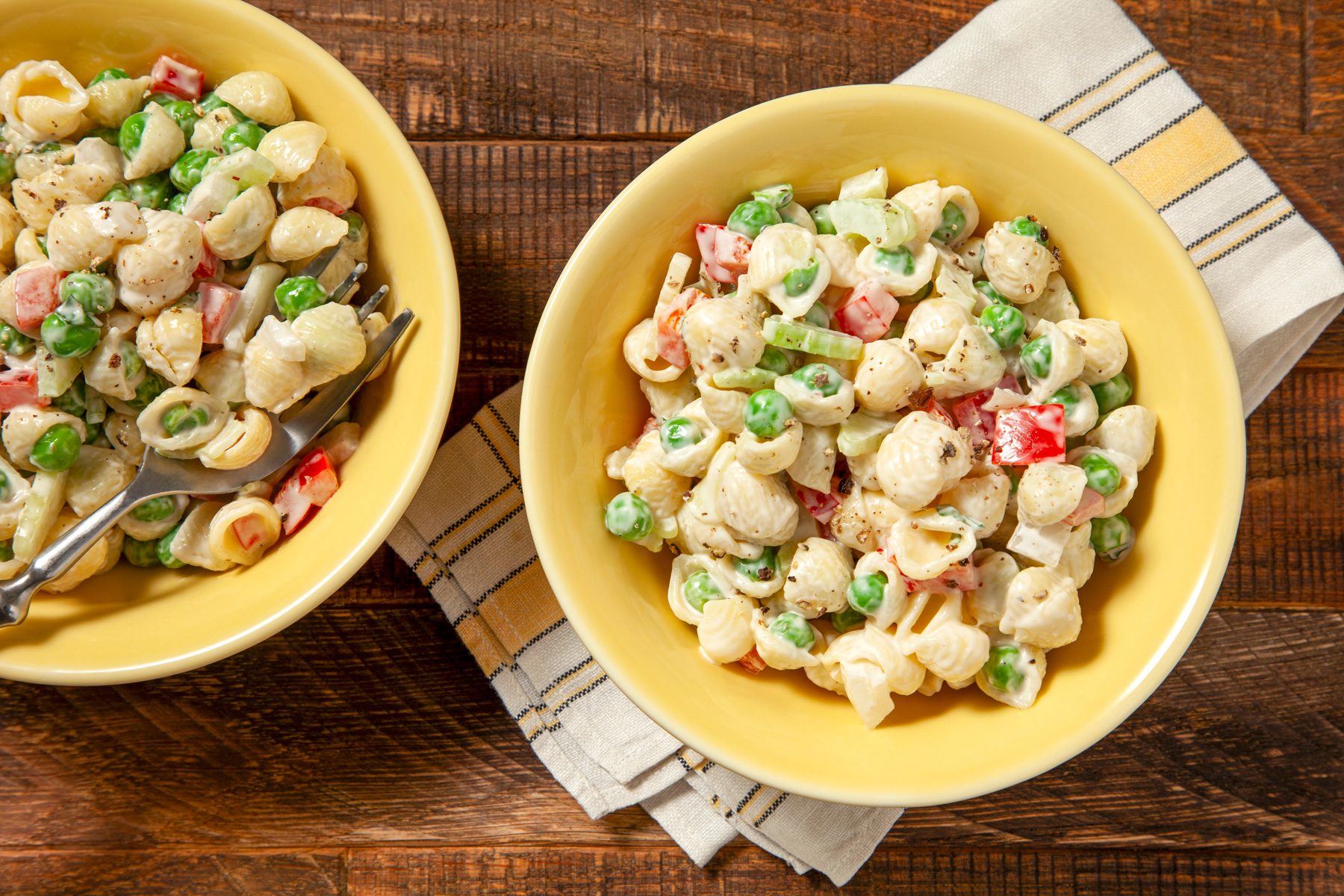 Two bowls of Pasta Salad With Peas, Pepper and Red Onions on wooden table