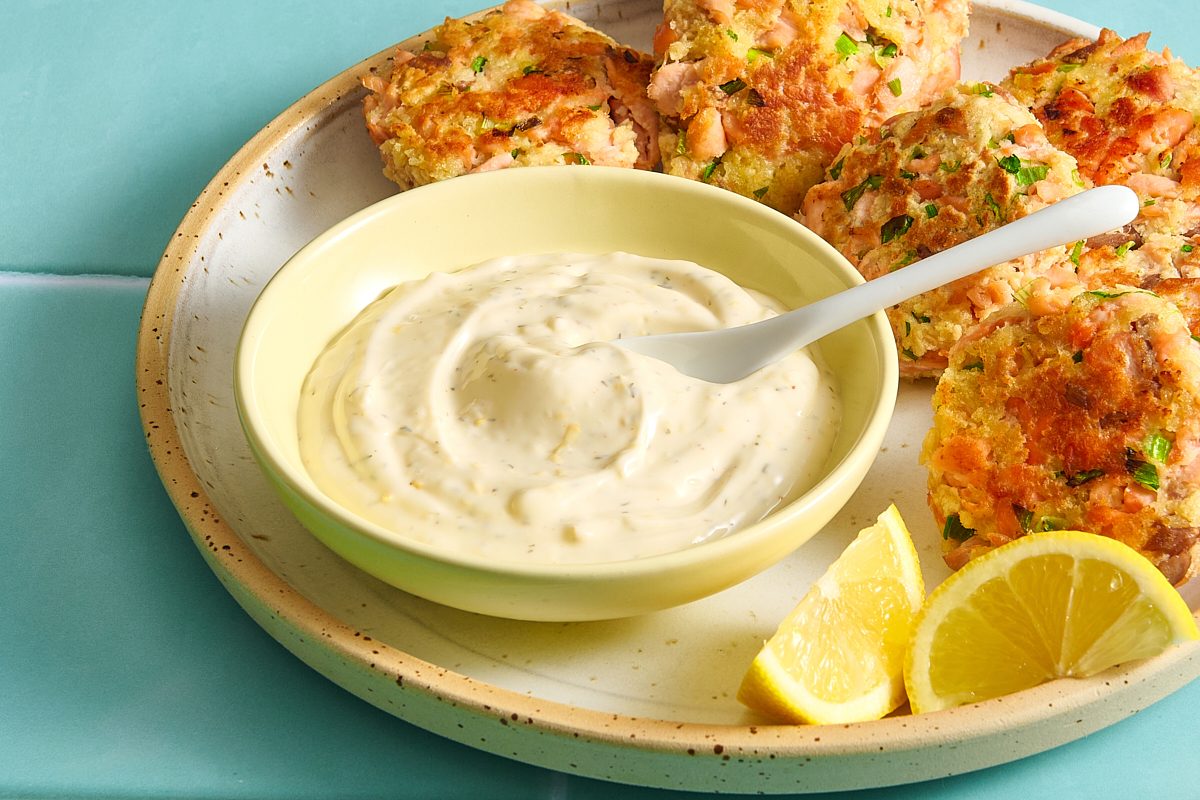 Closeup of salmon patty sauce in a bowl served with salmon patties and lemon wedges