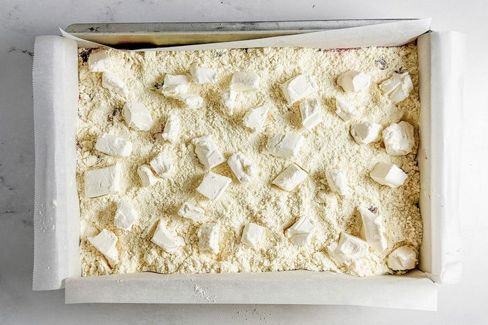 Cubed cream cheese and yellow cake mix in a metal baking pan for Taste of Home Strawberry Cheesecake Dump Cake.
