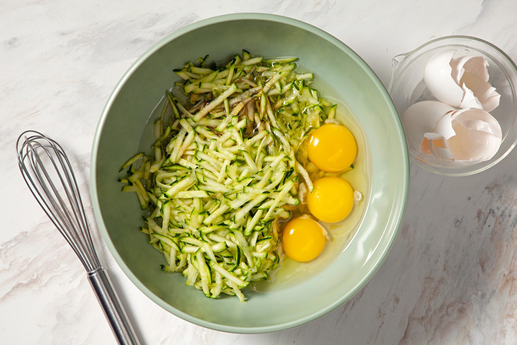 A bowl of zucchini noodles with eggs and a whisk