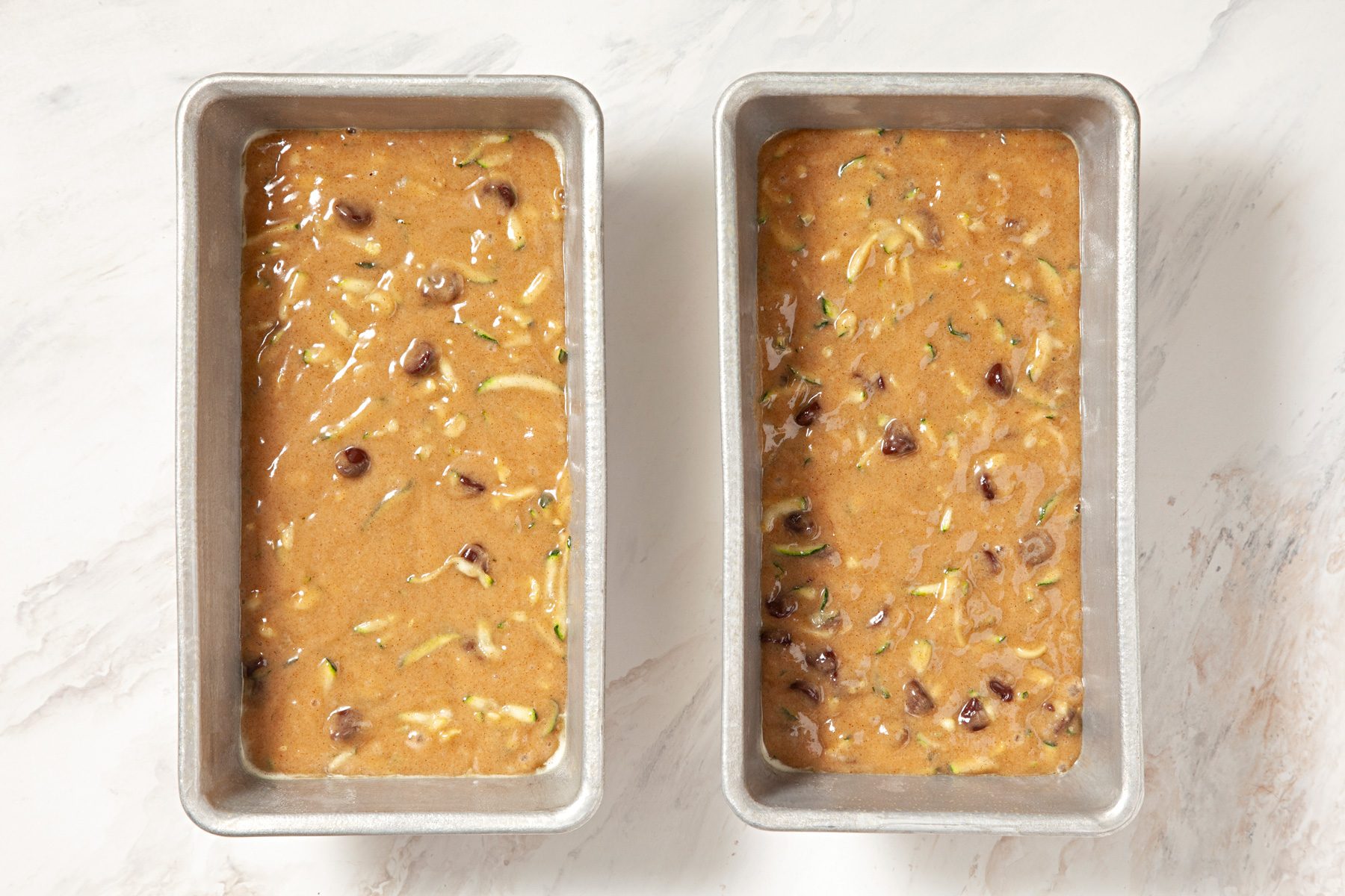 Two pans of batter with nuts and raisins, ready to be baked