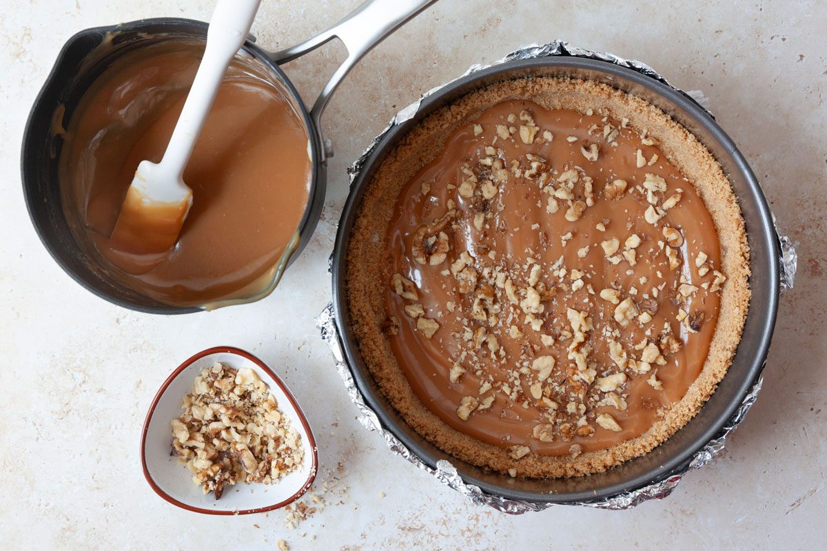 Step 3 of Taste of Home Caramel Apple Cheesecake is to make caramel sauce and spread it on the crust, then top with pecans