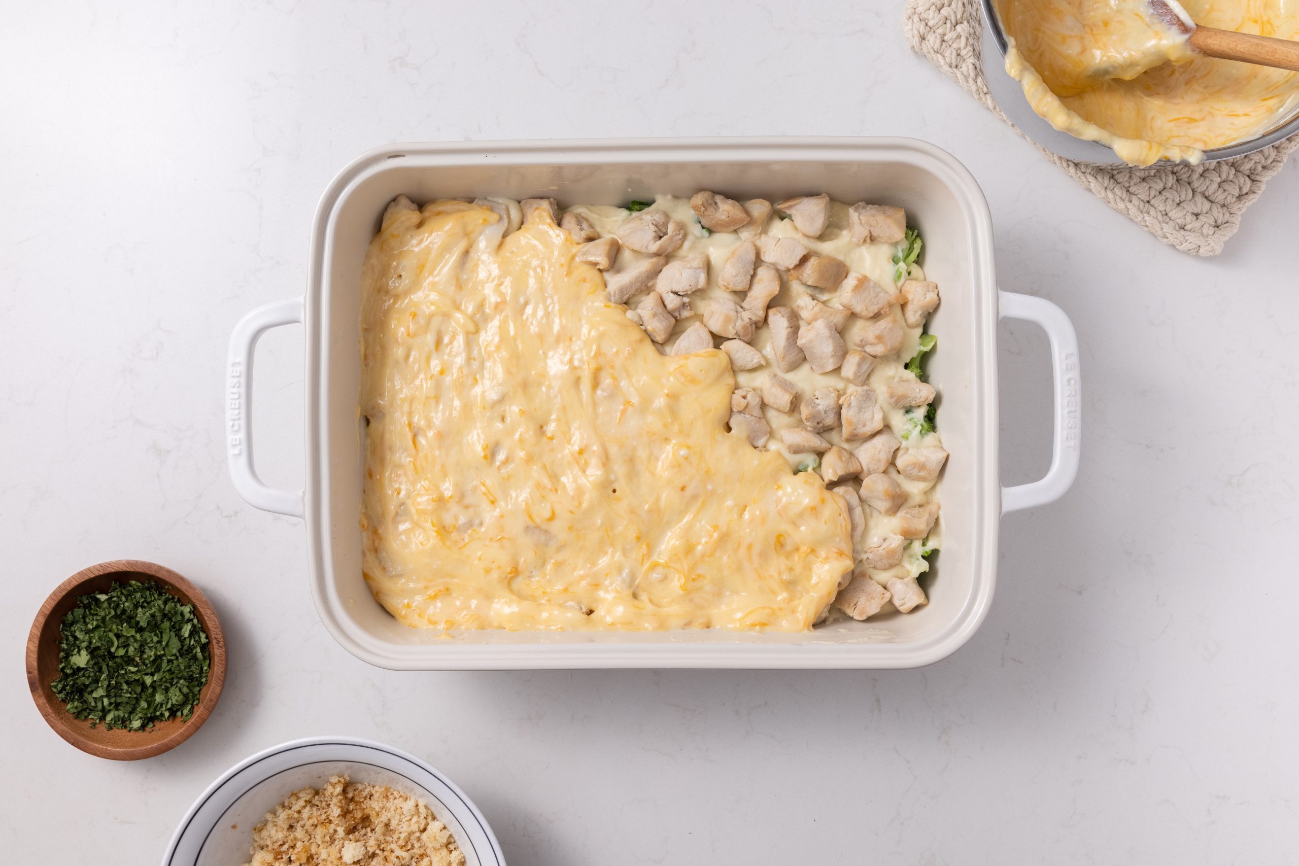 Casserole being assembled in layers on baking dish and sauce poured on top.