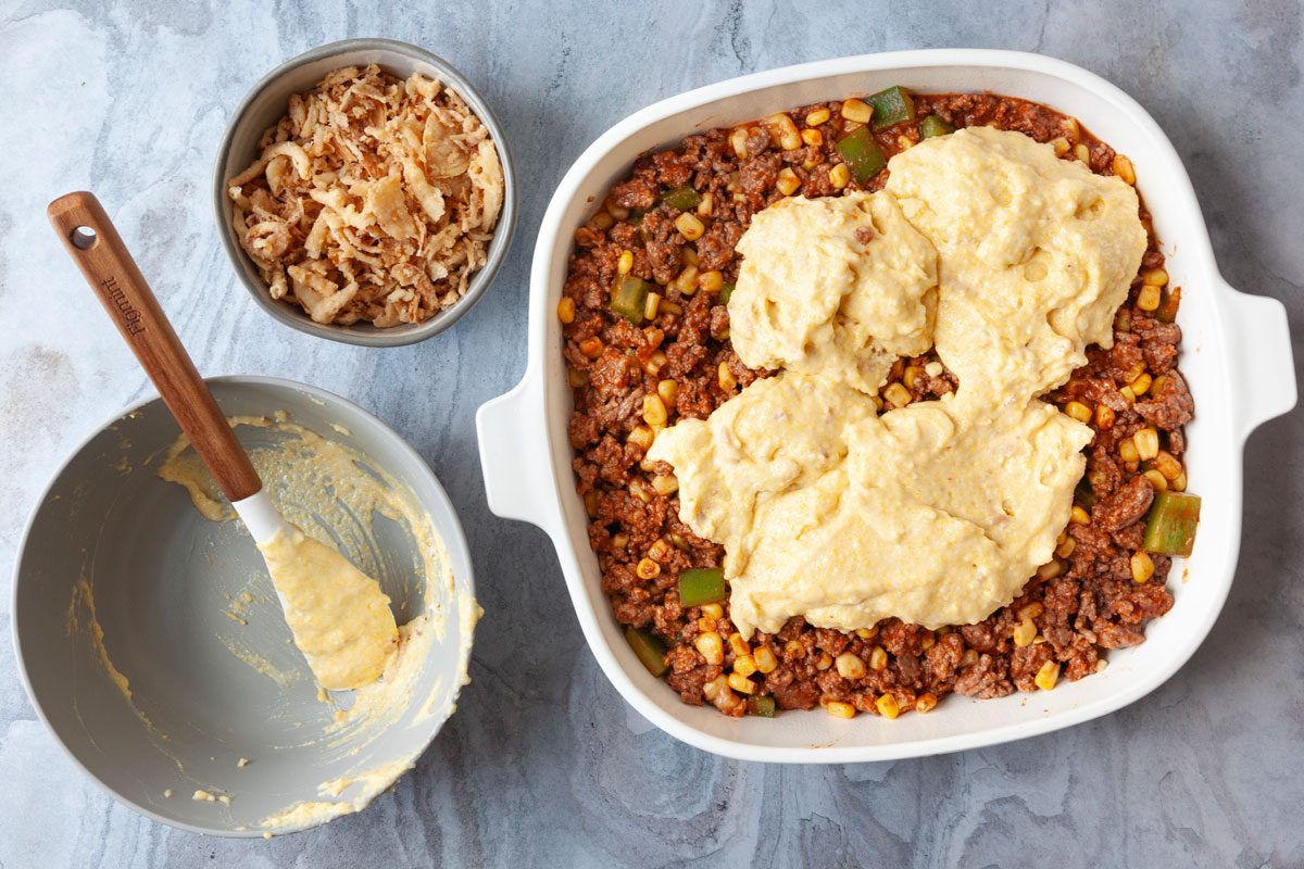 Step 2 of Taste of Home Cornbread Taco Bake is to add the beef mixture to a pan and top with cornbread mixture and french fried onions