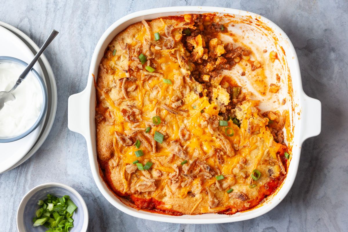 Full yield of Taste of Home Cornbread Taco Bake with a scoop out, topped with green onions