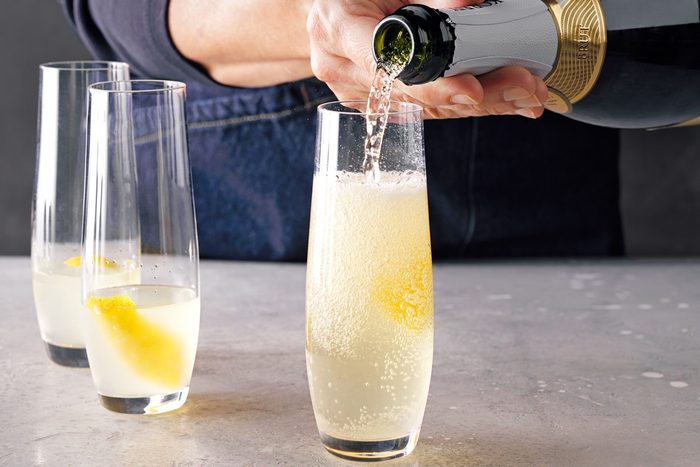 Table view shot of strain into champagne glass; Top with champagne; garnished with lemon peel; marble background;