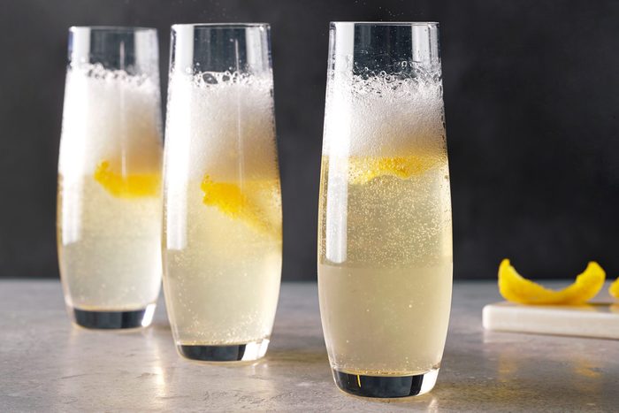 Table view shot of French 75 Cocktail; served in champagne glasses; garnished with lemon peel; chopping board; marble background;