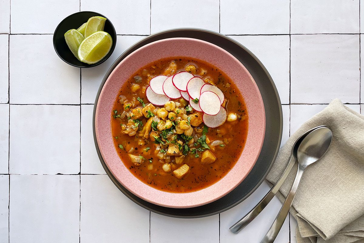 Overhead shot of Taste of Home's Hominy Soup in a pink bowl on a white tile background
