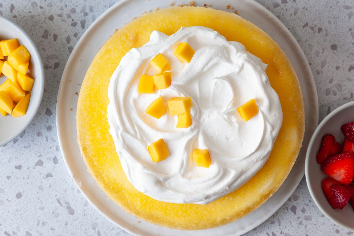 Step 5 of Taste of Home Mango Cheesecake is to garnish the cheesecake with whipped cream and additional mango and strawberries