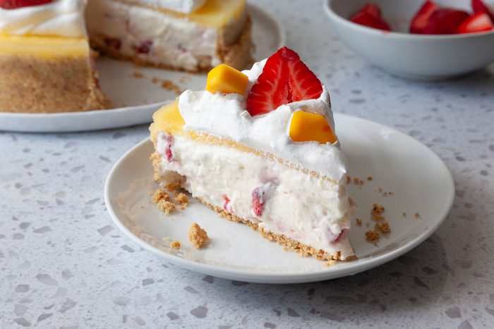 Single serving of Taste of Home Mango Cheesecake garnished with whiped cream, strawberries and mangoes