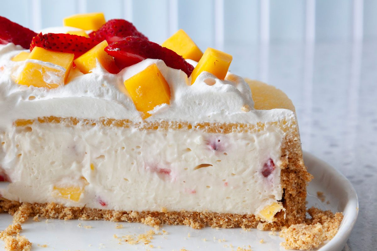 Close up of cut into full yield of Taste of Home Mango Cheesecake garnished with whiped cream, strawberries and mangoes