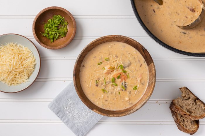 Seafood bisque bowl garnished with shredded cheese, green onions and bread on the side.