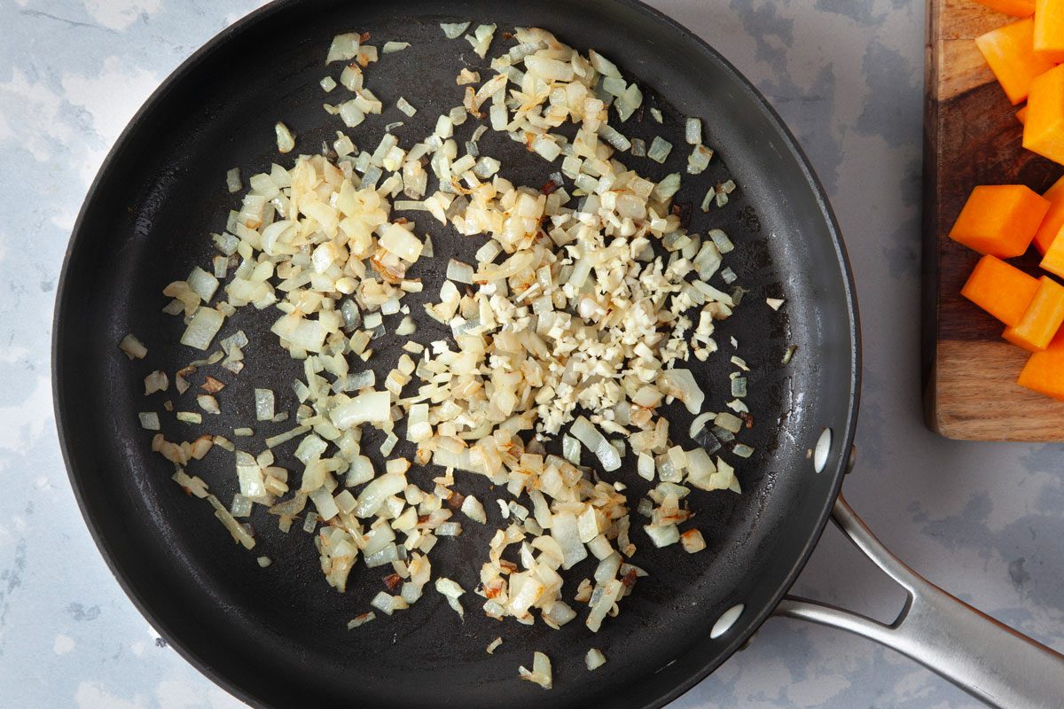 Sautéed onion and garlic in pan, butternut squash on cutting board