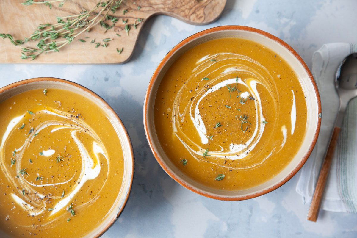 two single servings of butternut squash soup with a sour cream and fresh thyme garnish