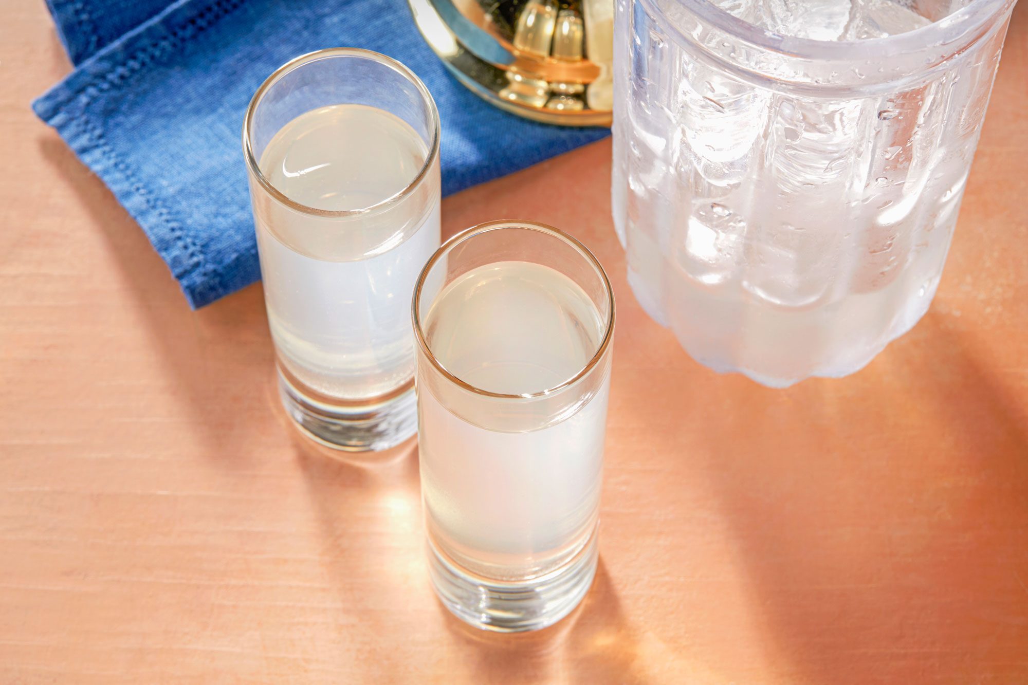 Overhead shot of White Tea Shots; served in two shot glasses; shaker; blue napkin; light orange background;