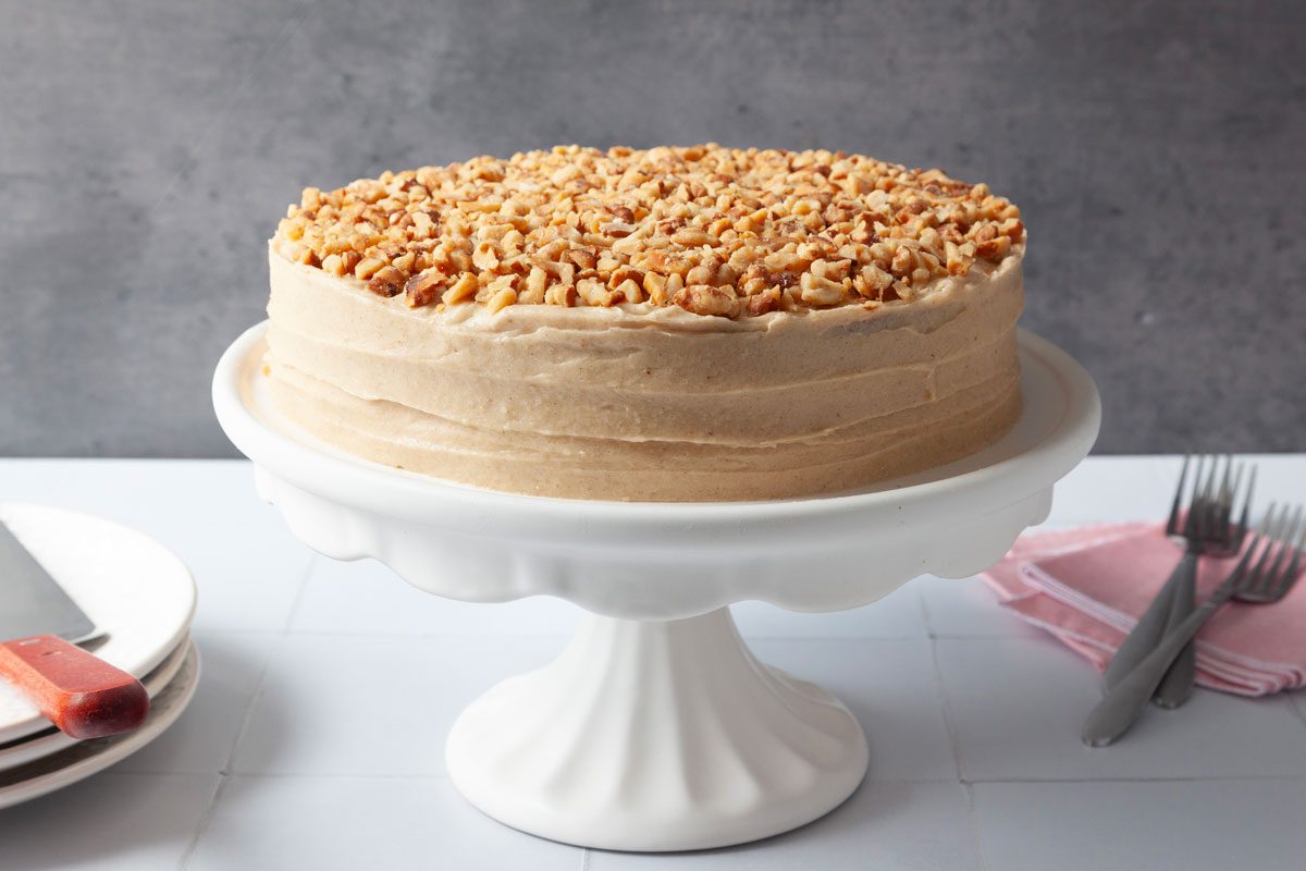 Full yield of Taste of Home Apple Spice Cake on a white cake stand, white serving plates