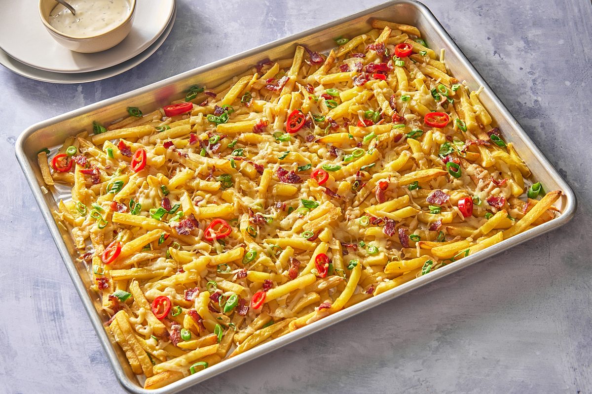 Bacon cheese fries on a large baking tray, served with ranch dressing on the side