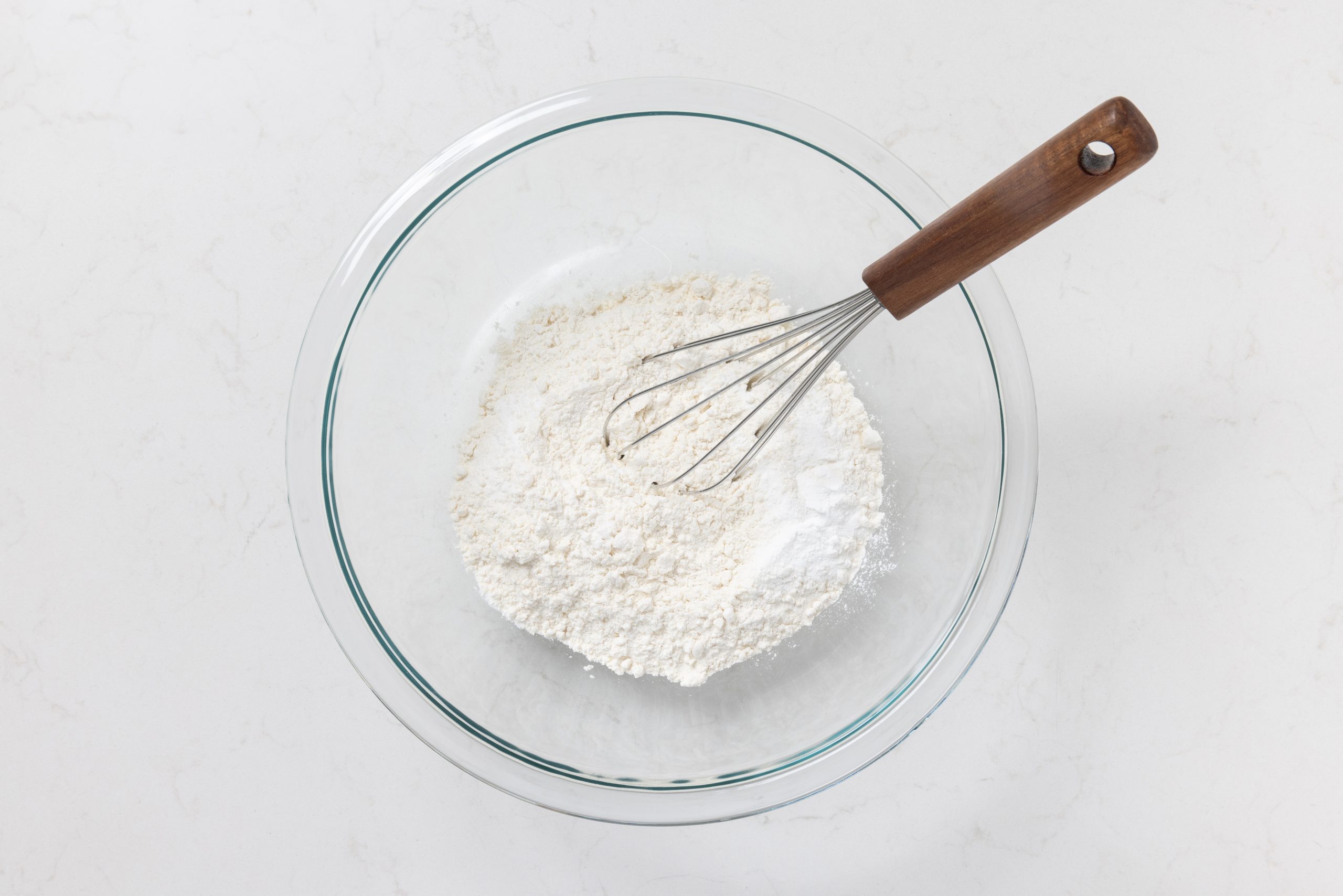 Flour, baking powder, baking soda and salt being mixed in bowl.