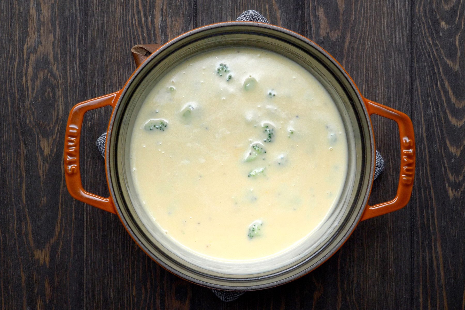 overhead shot; wooden background; Broccoli Cheddar Soup in a small saucepan;
