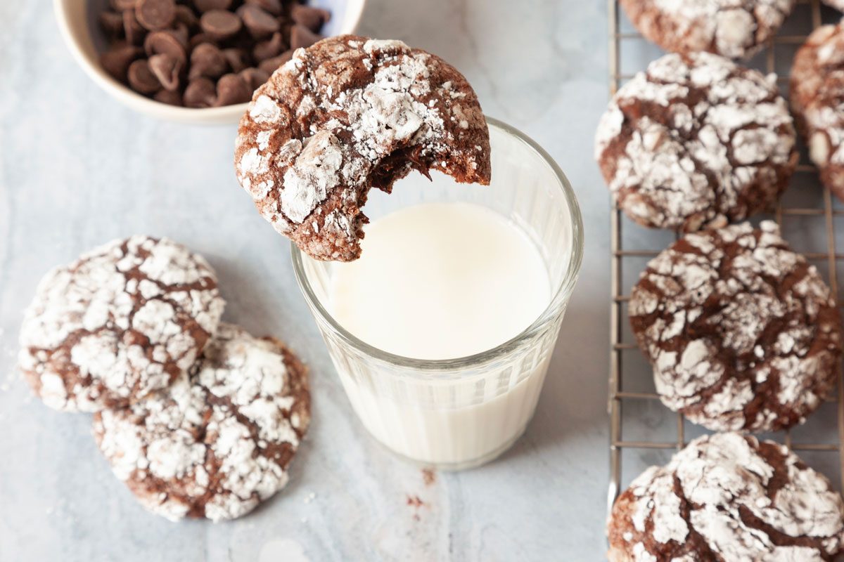 Taste of Home Brownie Mix Cookies on a cooling rack, one balanced on a cup of milk, chocolate chips peaking in