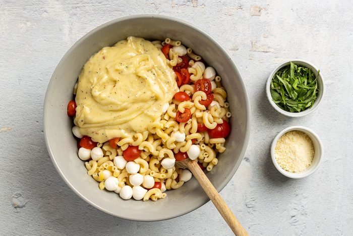 Taste of Home Caprese Pasta Salad recipe photo of all the ingredients in a bowl with basil and cheese on the side.