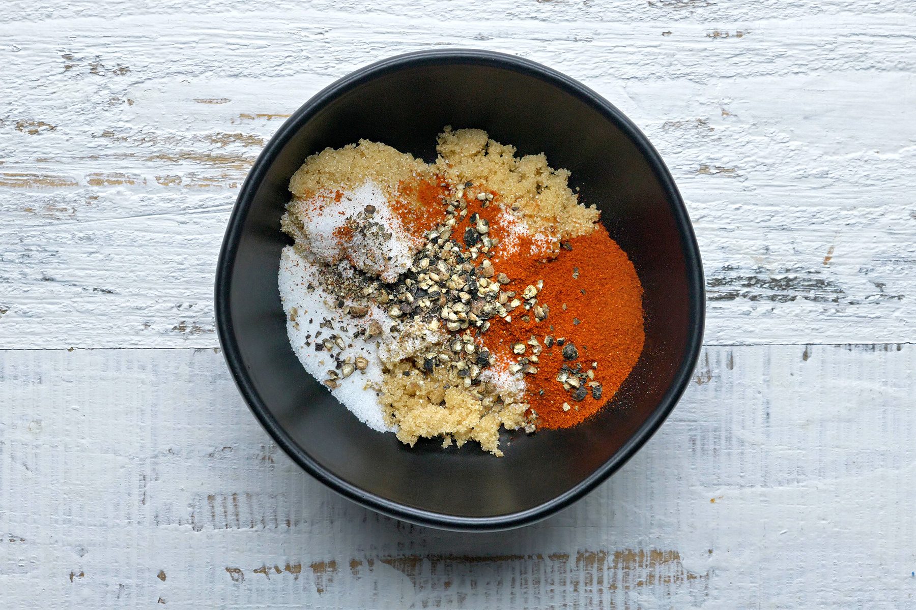 overhead shot; white textured background; in small black bowl, Mix brown sugar, salt, paprika and pepper;