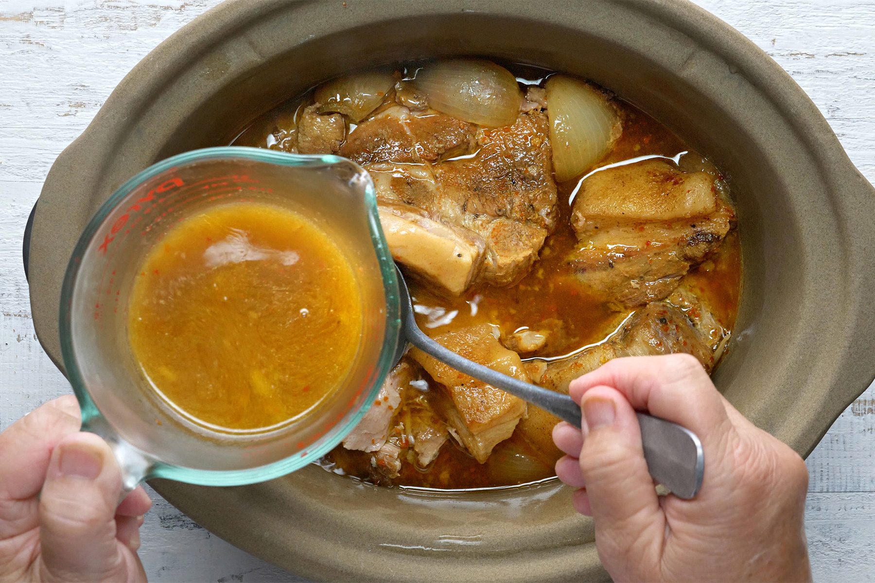 overhead shot; white textured background; adding reserve juice into the pork;